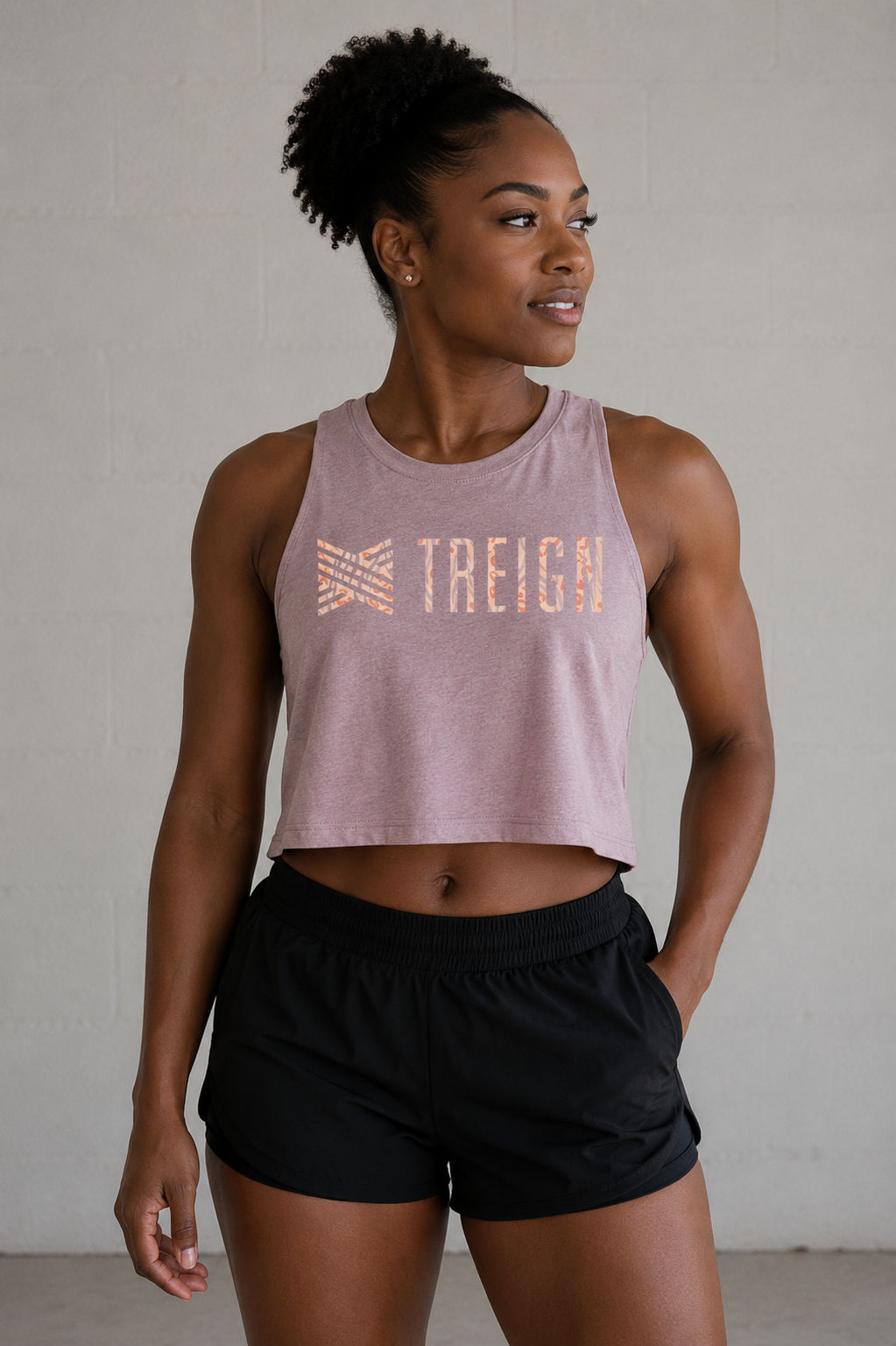Woman wearing a mauve tank top with 'TREIGN' branding and black shorts against a plain background